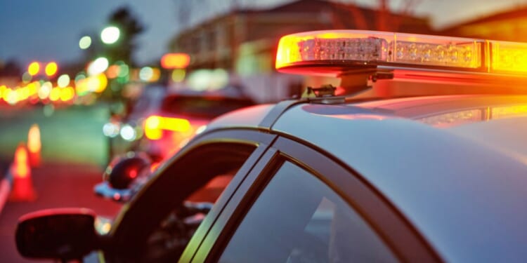 A police car sits alongside a road at night while its lights are flashing.