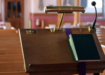 A modern wooden church pulpit with a light, microphone, and Bible on it.
