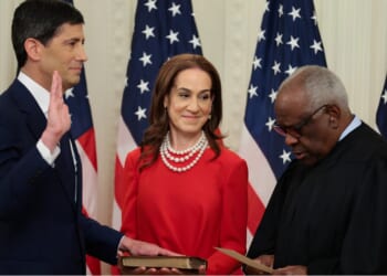 Kevin Warsh with his hand on a book with his wife Jane Lauder, and U.S. Supreme Court Associate Justice Clarence Thomas