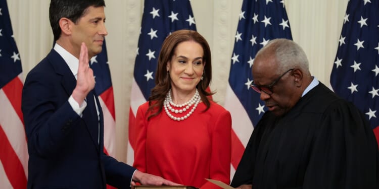 Kevin Warsh with his hand on a book with his wife Jane Lauder, and U.S. Supreme Court Associate Justice Clarence Thomas