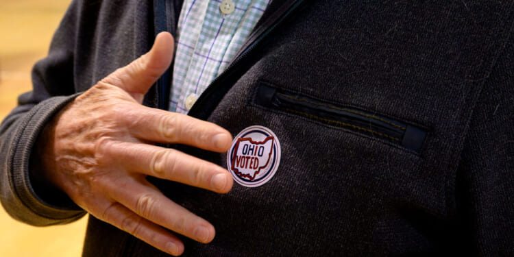 A man places his hand by the "Ohio Voted" sticker on his suit jacket.