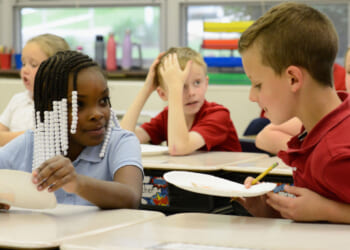 Children in school uniforms smile at each other as they hold white paper plates.