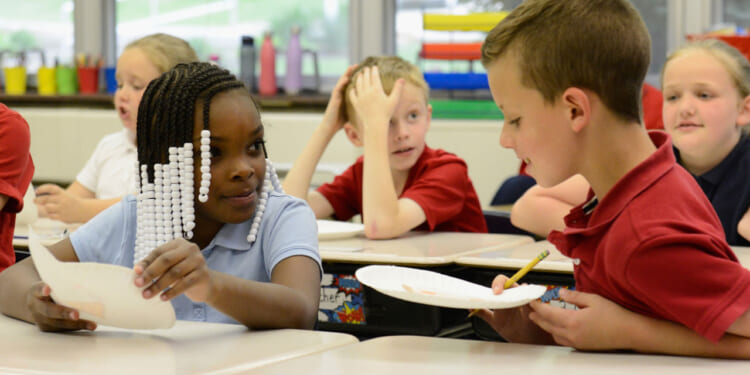 Children in school uniforms smile at each other as they hold white paper plates.
