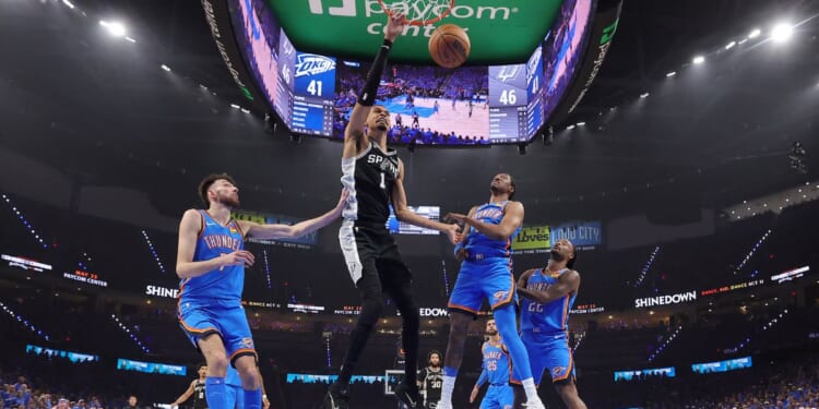 Victor Wembanyama of the San Antonio Spurs dunks the ball between Chet Holmgren and Jalen Williams of the Oklahoma City Thunder during the first half in Game One of the NBA Western Conference Finals at Paycom Center on May 18, 2026, in Oklahoma City, Oklahoma.