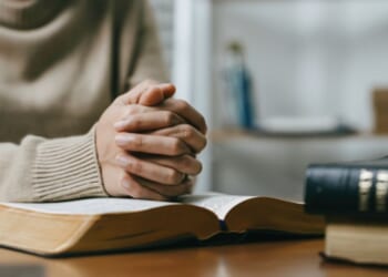 Woman prays with her hands on a Bible.