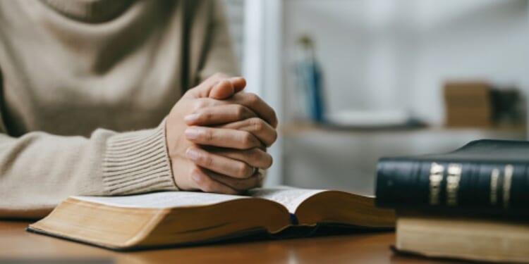 Woman prays with her hands on a Bible.