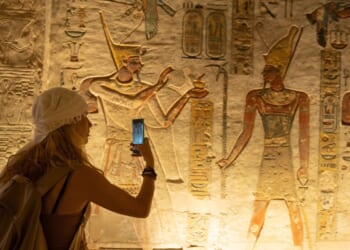 A woman holds out her smartphone and takes a picture of ancient depiction of Ramses IX at the Valley of Kings in Luxor, Egypt.