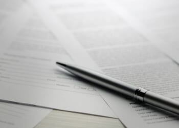 Papers are strewn across a table with a pen laying on top of them all.