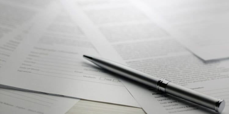 Papers are strewn across a table with a pen laying on top of them all.