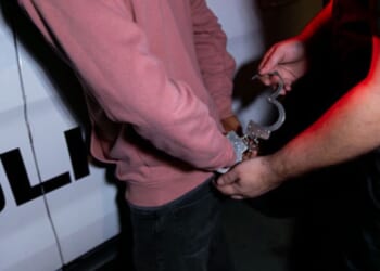 A man is arrested while pressed against a police car.