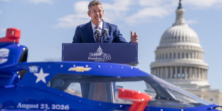 Transportation Secretary Sean Duffy speaking at a podium in front of a car