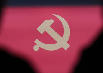 The communist emblem is seen framed by the silhouettes of two people during a press conference of the Central Committee of the Communist Party of China (CPC).