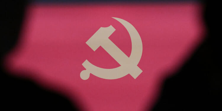 The communist emblem is seen framed by the silhouettes of two people during a press conference of the Central Committee of the Communist Party of China (CPC).