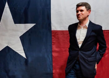 Texas State Senator James Talarico strikes a pose in front of a Texas flag.