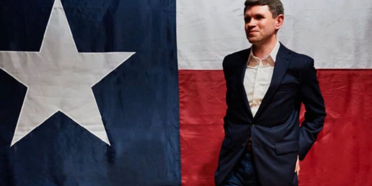 Texas State Senator James Talarico strikes a pose in front of a Texas flag.