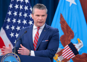 Secretary of War Pete Hegseth at a podium briefing reporters.