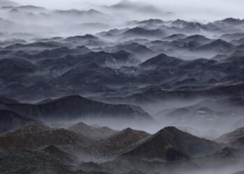 Mountains stand in swaths of fog.