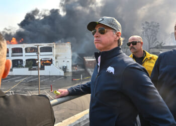 Gavin Newsom, in sunglasses and grey cap overlooks the Pacific Palisades fire.