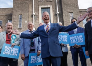 Nigel Farage smiling surrounded by Reform UK party members