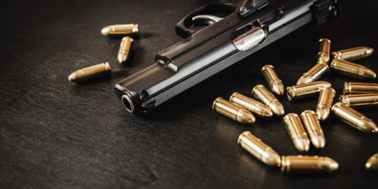 A gun lays on a table near dozens of bullets.