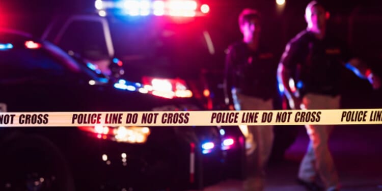 Police lights flash at a crime scene as two officers walk by.