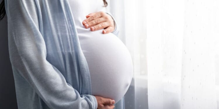A pregnant woman holds her stomach as she looks out a mirror.