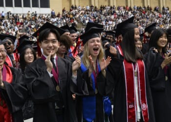 Graduates in robes clapping, cheering, and smiling