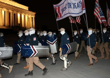 Members of the white nationalist group Patriot Front, wearing masks and carrying shields, gather at the Lincoln Memorial at night.