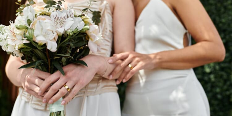 Two women dressed as brides stand close to each other as one embraces the other.