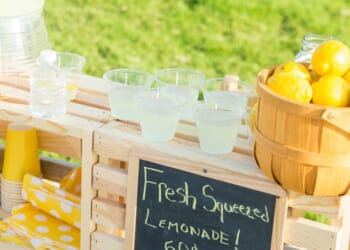A lemonade stand is set up in the front yard of a home in the suburbs.