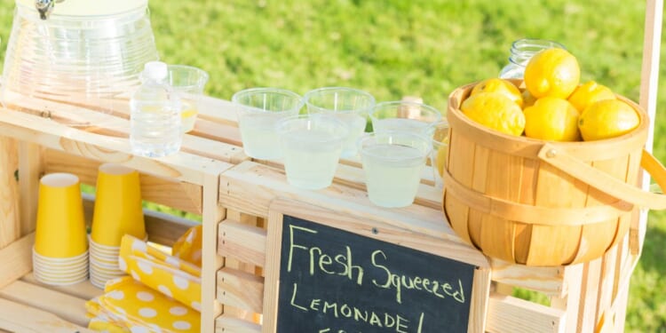 A lemonade stand is set up in the front yard of a home in the suburbs.