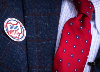 A man's navy suit with red and blue tie features an "OHIO VOTED" sticker.