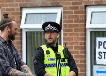 A police officer stands on duty as people arrive to cast their vote in the Makerfield by-election, at a polling station set up at a Library in Winstanley, part of the Makerfield parliamentary constituency, in northwest England on June 18, 2026.