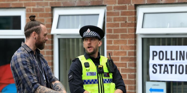 A police officer stands on duty as people arrive to cast their vote in the Makerfield by-election, at a polling station set up at a Library in Winstanley, part of the Makerfield parliamentary constituency, in northwest England on June 18, 2026.