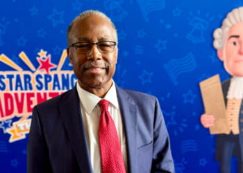Dr. Ben Carson stands in front of a backdrop promoting his movie.