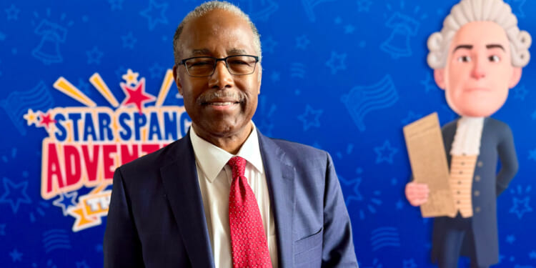 Dr. Ben Carson stands in front of a backdrop promoting his movie.