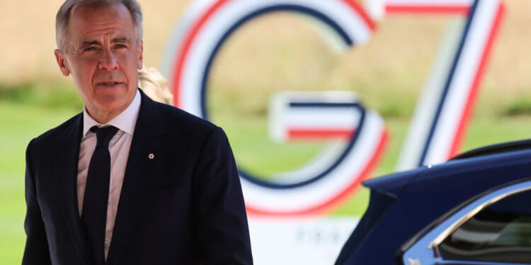 Canadian Prime Minister Mark Carney walks with G7 sign behind him.