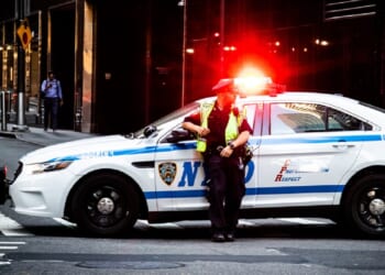A New York City police officer is pictured in a May 2019 file photo with his patrol vehicle's lights flashing.
