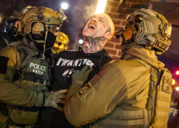Federal agents with Homeland Security Investigations (HSI) detain a protestor wearing an "Antifa" shirt.