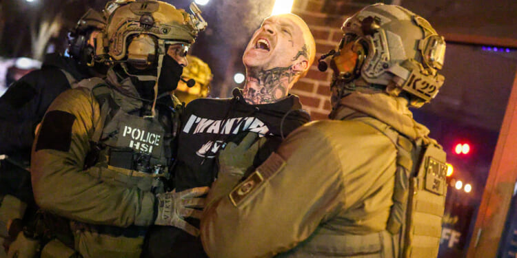Federal agents with Homeland Security Investigations (HSI) detain a protestor wearing an "Antifa" shirt.