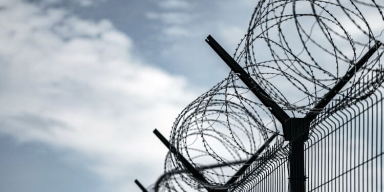 A prison with razor wire against a dark sky.