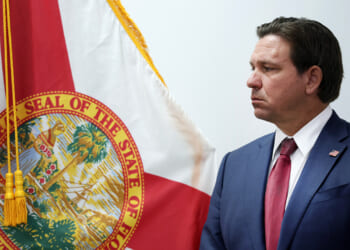 Governor Ron DeSantis standing in front of Florida flag.