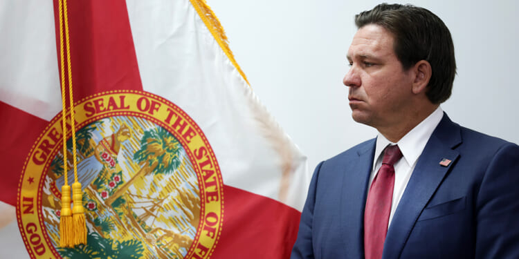Governor Ron DeSantis standing in front of Florida flag.
