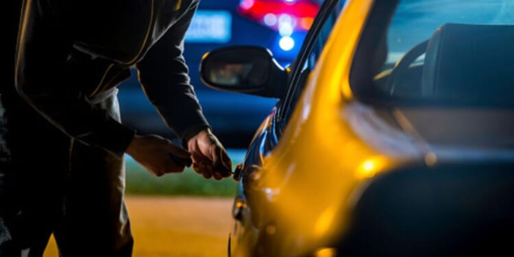 A man tries to pick a lock on a car.