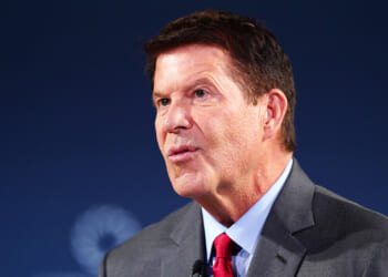 Keith Krach speaking in front of a blue background.