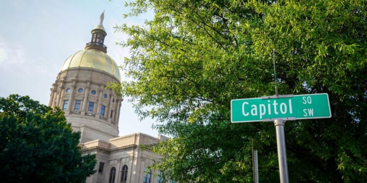 The Georgia State Capitol building is featured with trees and a street sign that says Capitol Square SW.