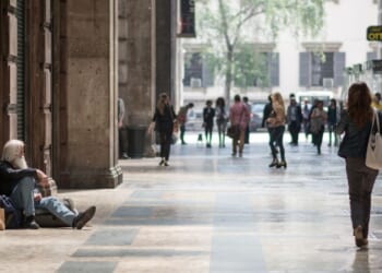 A homeless man sit in the street watching people passing by in Milan, Italy, on May 7, 2015.