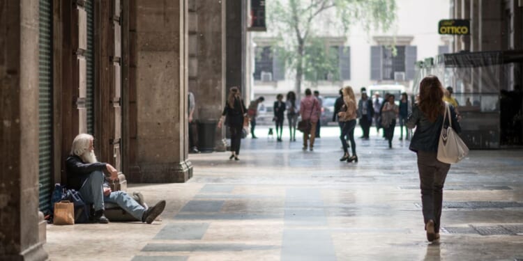 A homeless man sit in the street watching people passing by in Milan, Italy, on May 7, 2015.