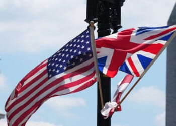 The United States flag and United Kingdom flag wave together on a light pole.