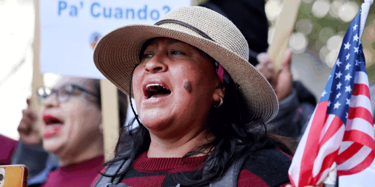 A hispanic woman protests in the street while holding an American flag.